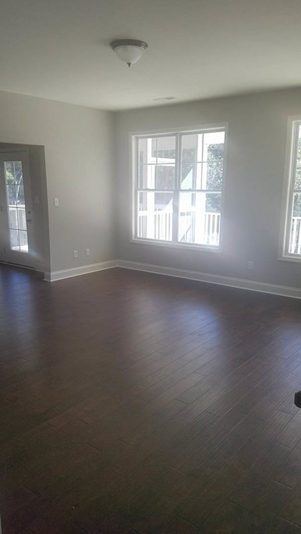 Room with dark wood flooring, white walls and baseboards, large windows with white frames, glass-paneled white door, and ceiling light fixture