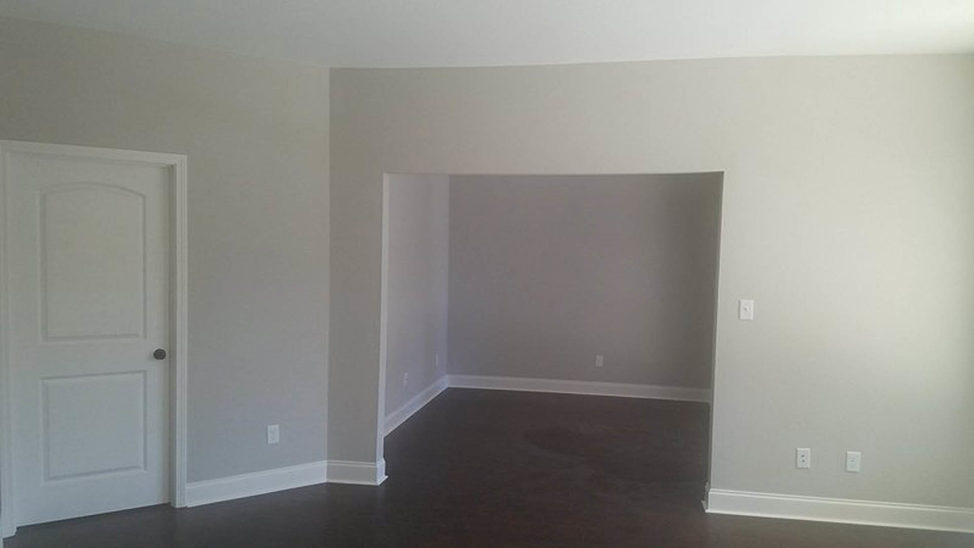 White paneled door with silver knob set in a grey wall, laminate flooring, white ceiling, and black baseboard molding