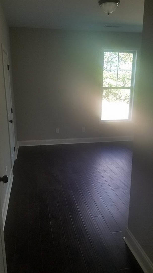 Sunlit room featuring a large window with a white frame, dark wood laminate flooring, white baseboard trim, and smooth plaster walls.