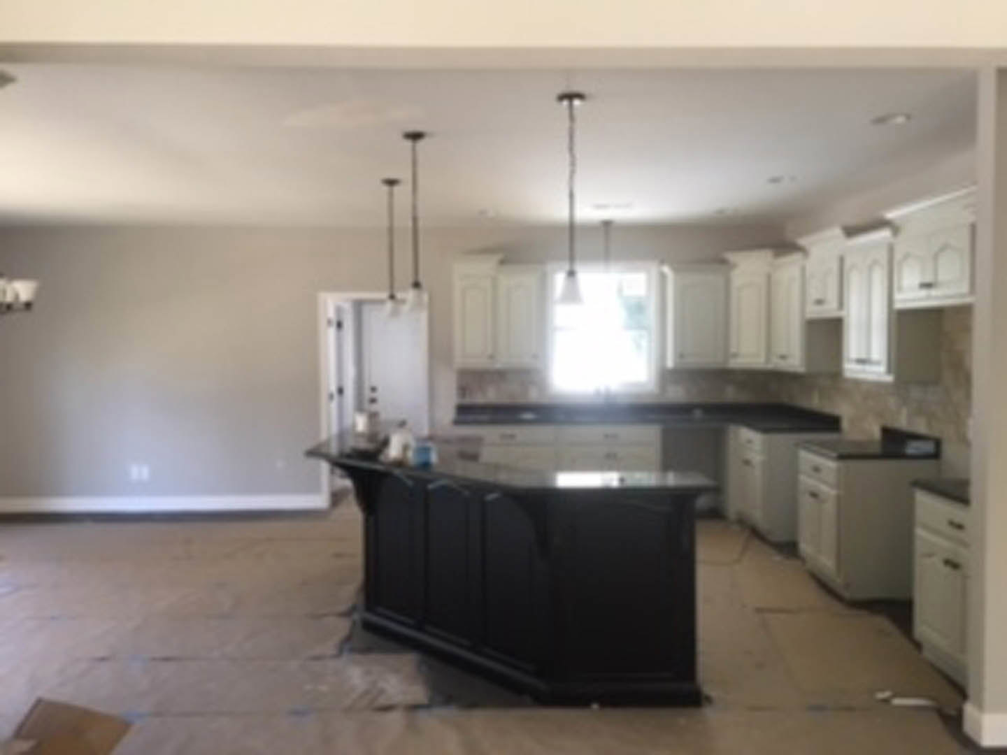 Black kitchen island with white countertop, light wood flooring, white cabinetry, stainless steel sink, and modern appliances