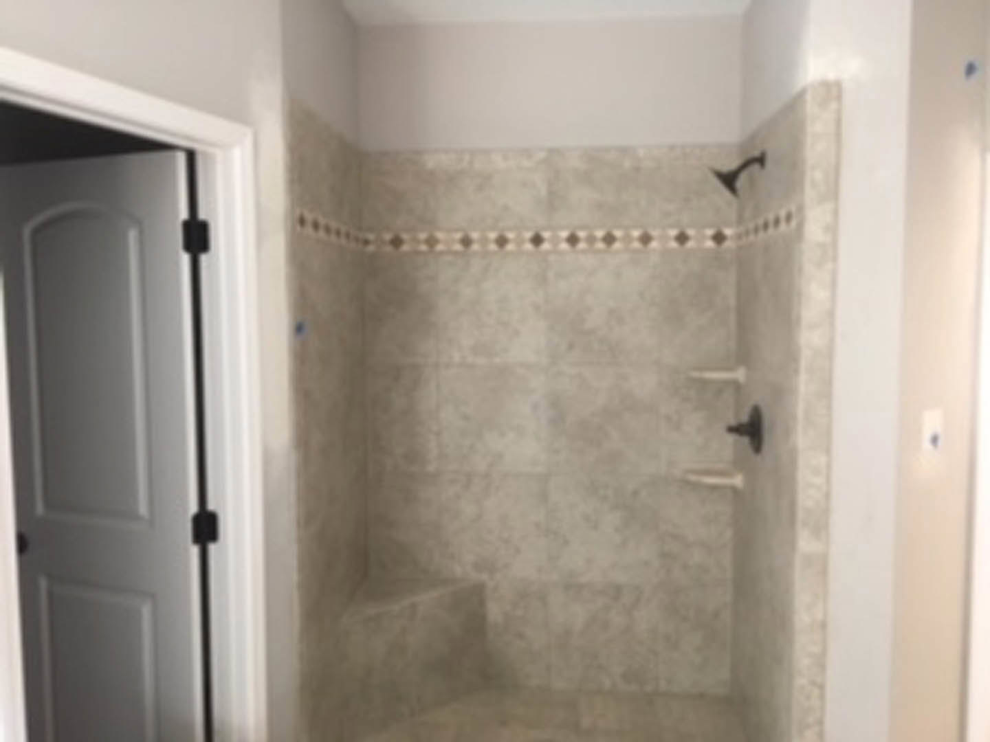 Walk-in shower with gray tile walls, glass door, chrome fixtures, and built-in niche for toiletries