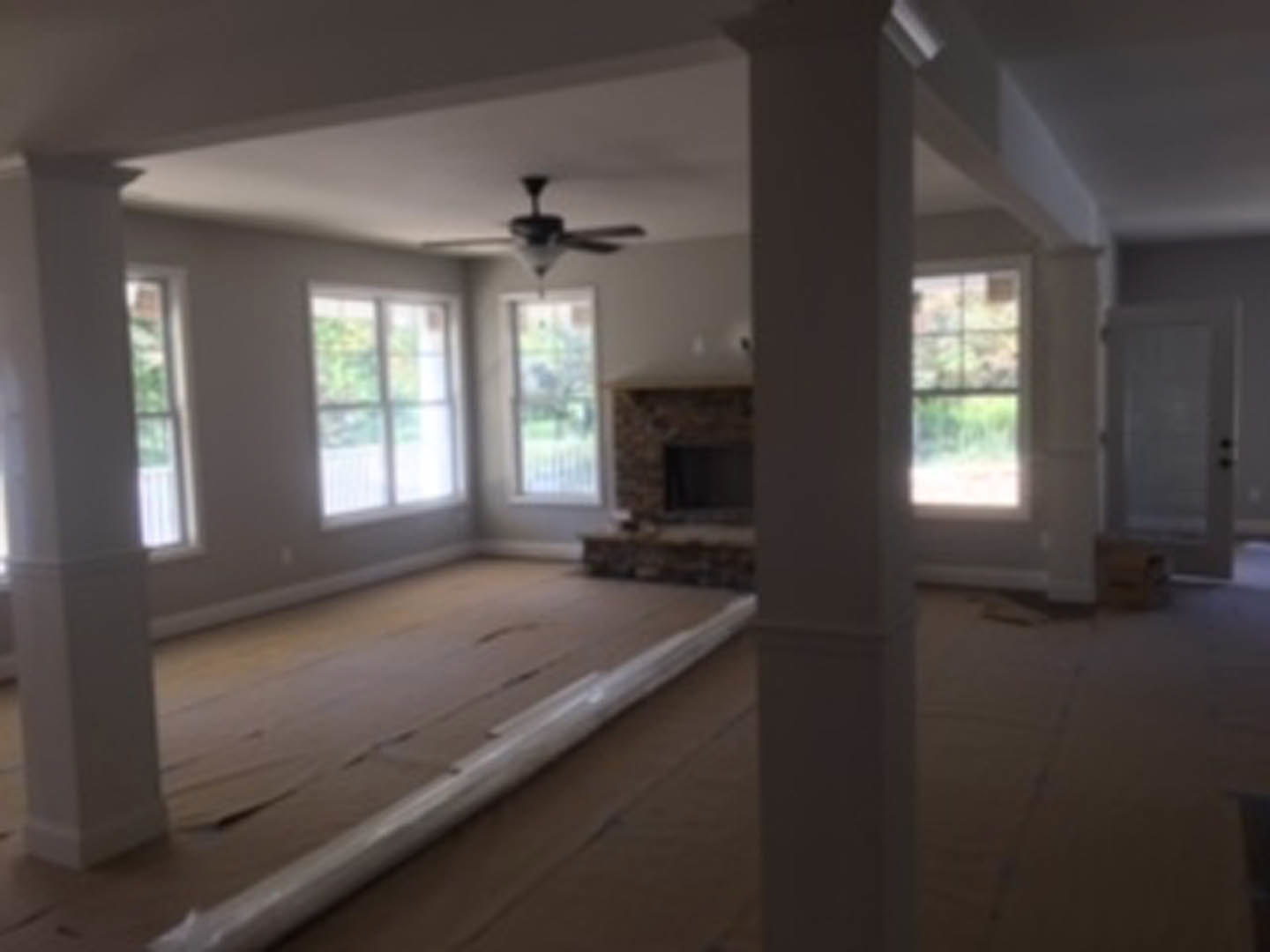 Living room featuring a stone fireplace, wood flooring, large windows, and a ceiling fan with light fixture