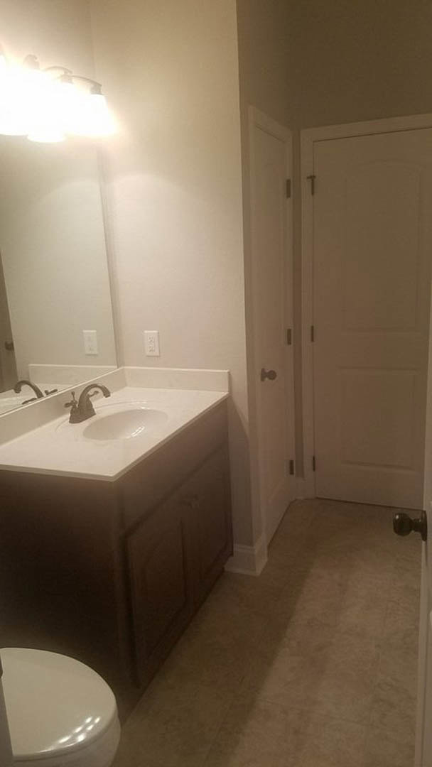 White tile bathroom featuring a rectangular sink with chrome faucet, large wall mirror, and partial view of a modern toilet and bathtub.