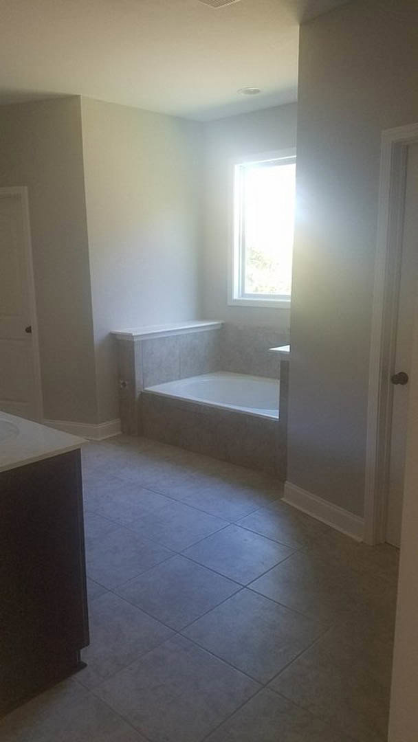 Freestanding white bathtub beneath a large window, black tile flooring, plaster walls, minimalist bathroom design