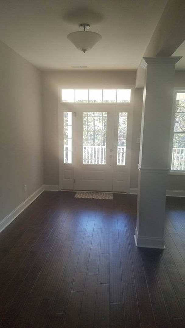White paneled door with glass panes, dark wood flooring, white walls, large window, and ceiling-mounted white light fixture
