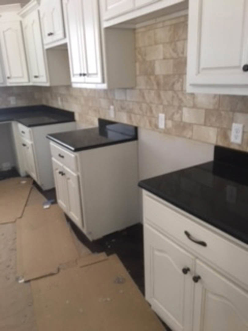 White kitchen cabinets with sleek black countertops, stainless steel appliances, light tile flooring, and recessed lighting