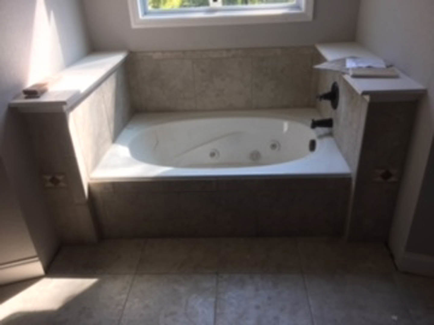Freestanding white bathtub with chrome faucet against tiled bathroom wall, glass shower enclosure, and light-colored flooring