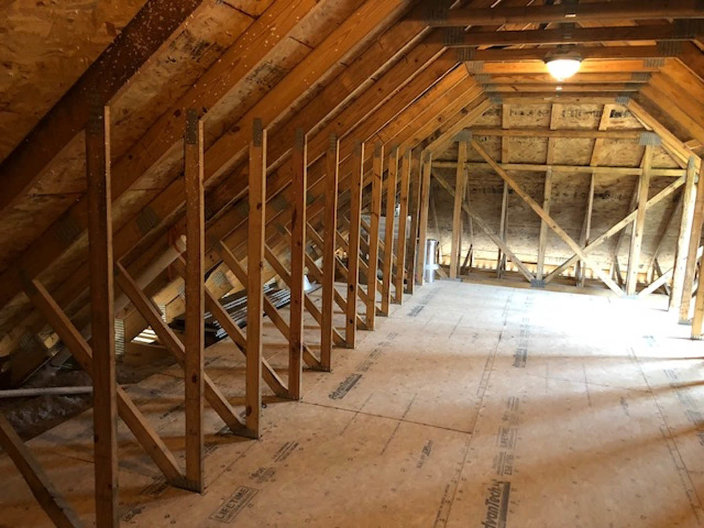Exposed wooden ceiling beams above a spacious attic room with unfinished wood flooring and visible insulation