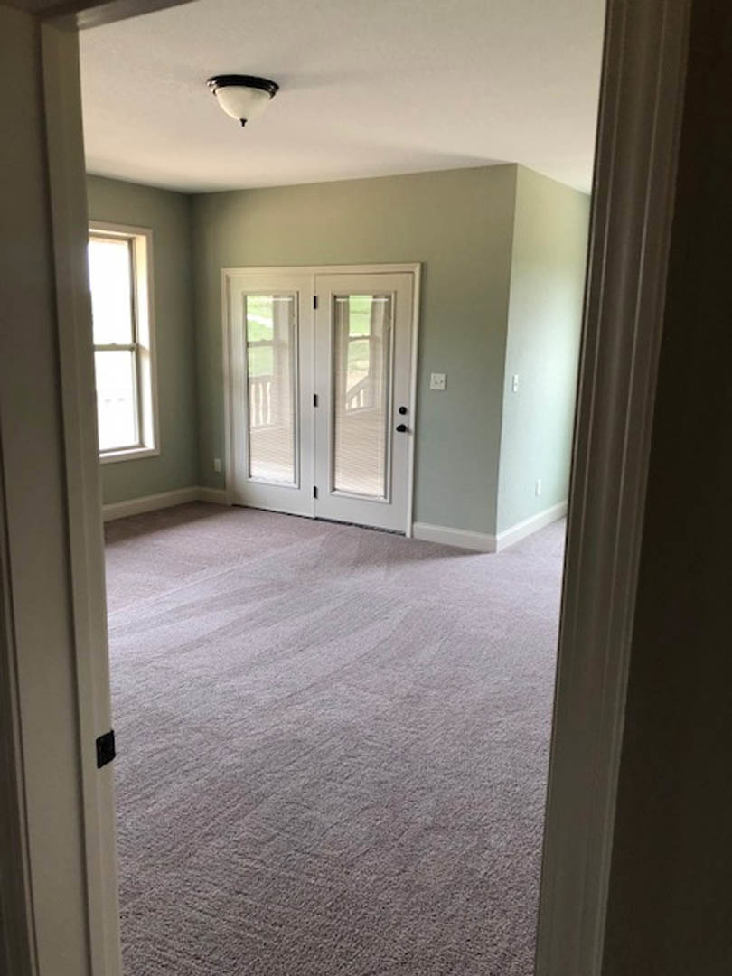 Carpeted room with double glass doors, white window frame, sunlight streaming through, light fixture, white walls with plaster and molding