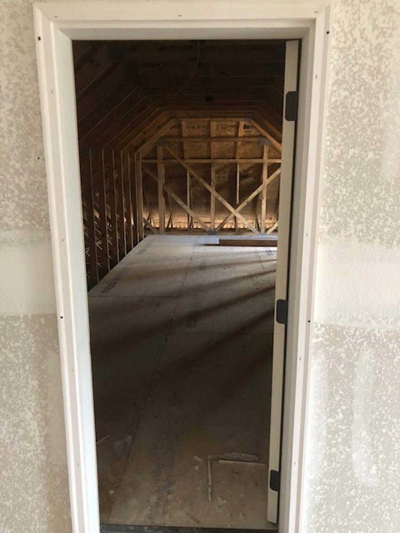 Open doorway framed by plaster walls, leading into a room with wooden ceiling beams and light-colored flooring