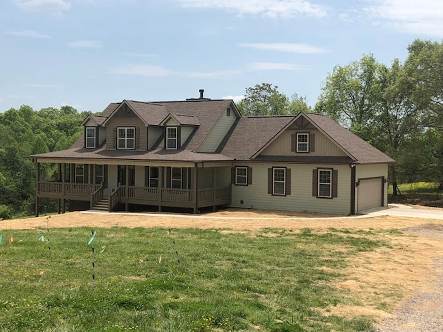Two-story house with white siding, covered front porch, large windows with white frames, manicured green lawn, mature trees in the background, blue sky with scattered clouds