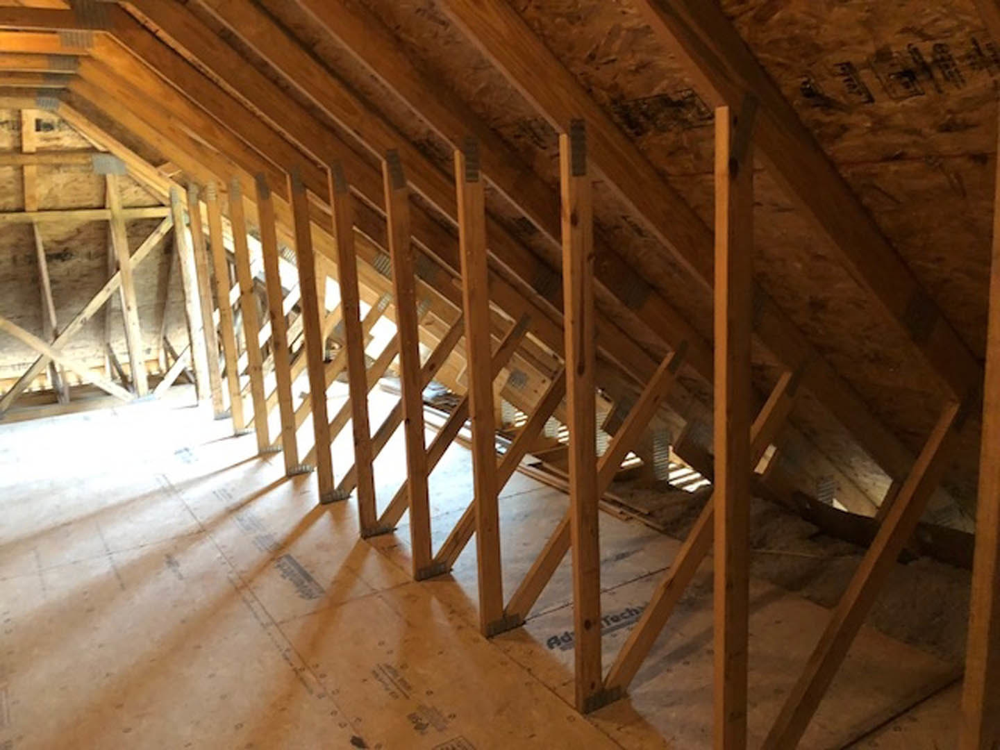 Exposed wooden beams and planks in an unfinished attic with visible insulation and hardwood surfaces