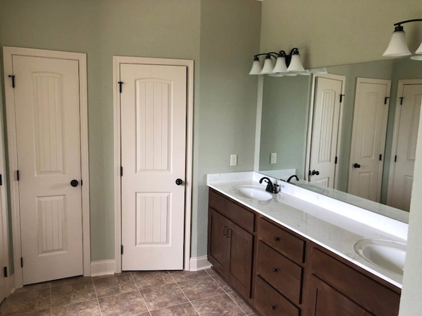 Bathroom with double vanity, white sinks, two doors, light tile flooring, white cabinetry, chrome faucets, and neutral wall finishes