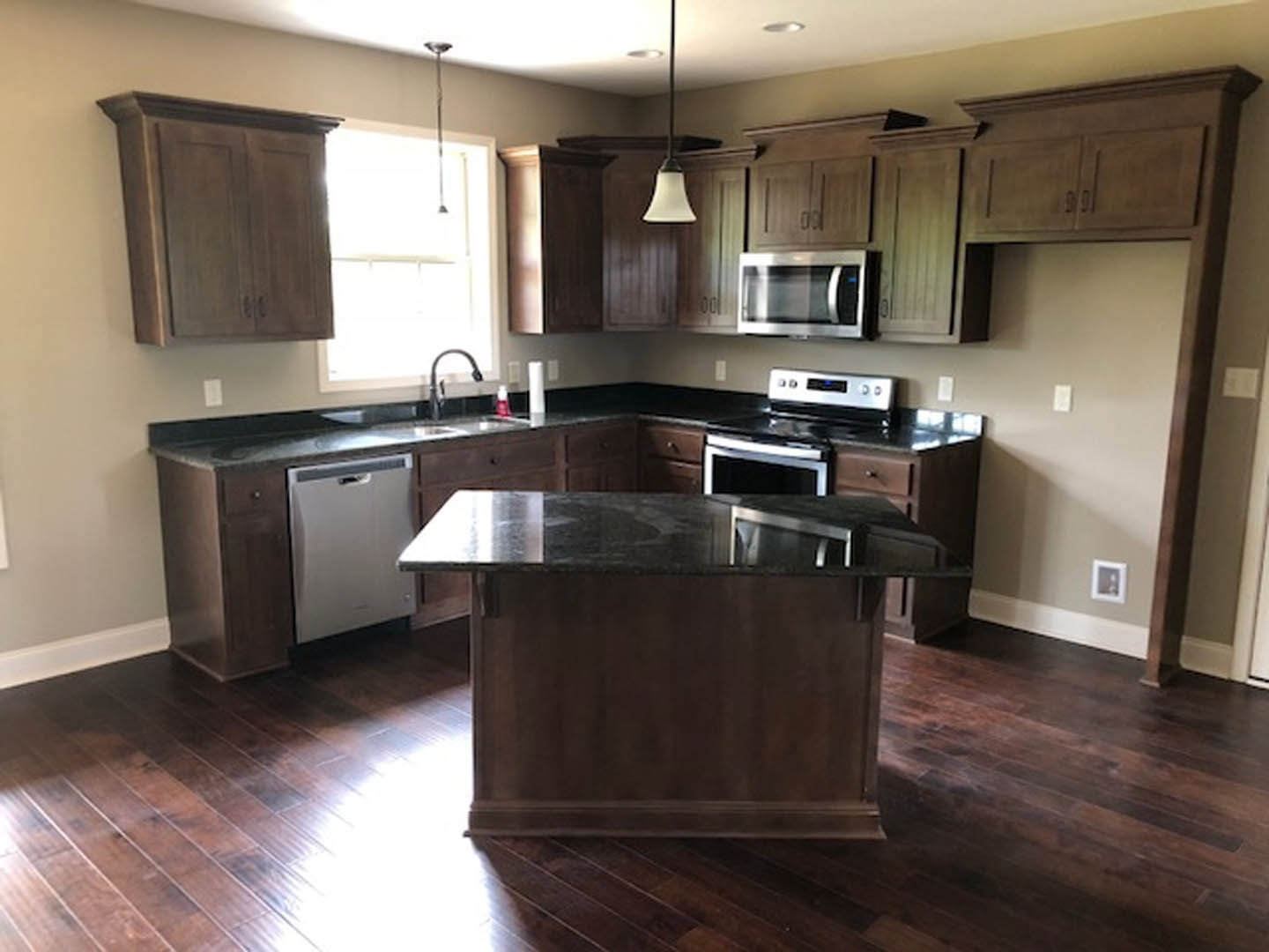 Open kitchen with wood flooring, central island featuring black marble countertop, white cabinetry, stainless steel stove and oven, white refrigerator, microwave, and decorative
