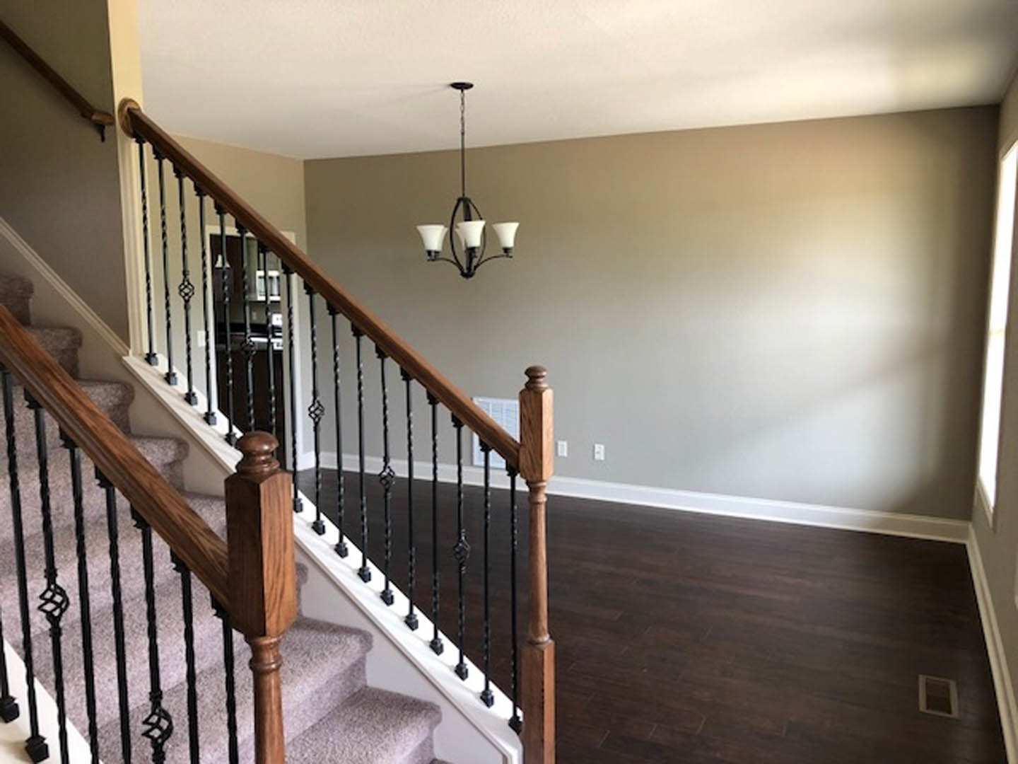 Curved staircase with dark wood steps, white risers, wooden post and railing, chandelier overhead, white trim, and nearby window with vent