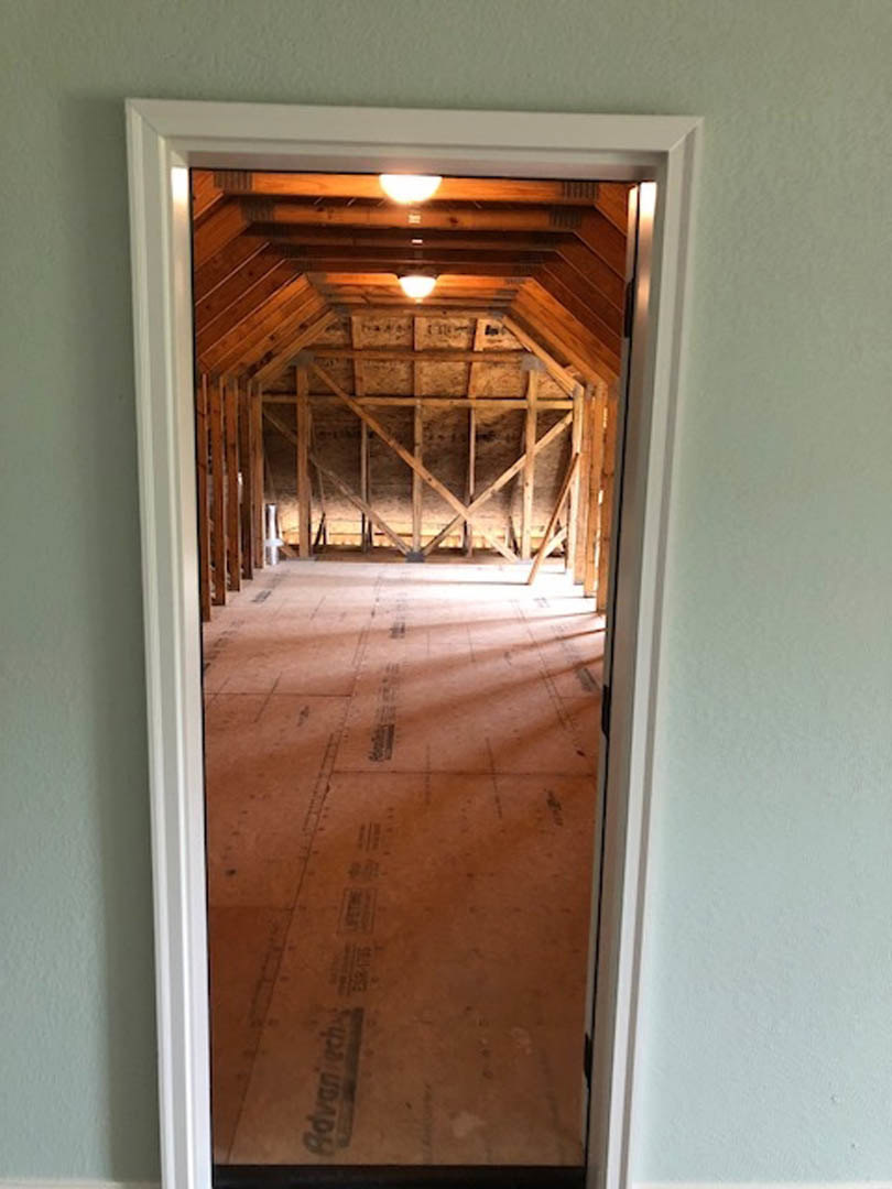 Wood-framed doorway opening to a room with plaster walls, exposed wood ceiling beams, and natural daylight streaming through a window.