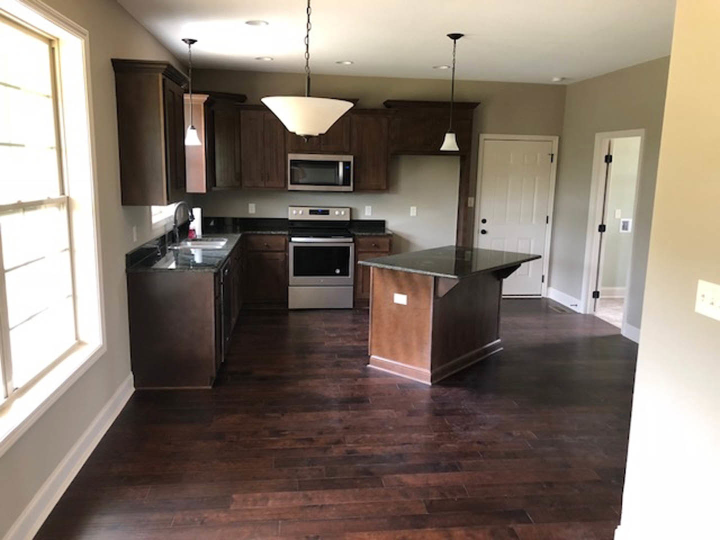 Kitchen with dark wood flooring, large central island with marble countertop, white cabinetry, stainless steel microwave, sink, and black hardware on doors