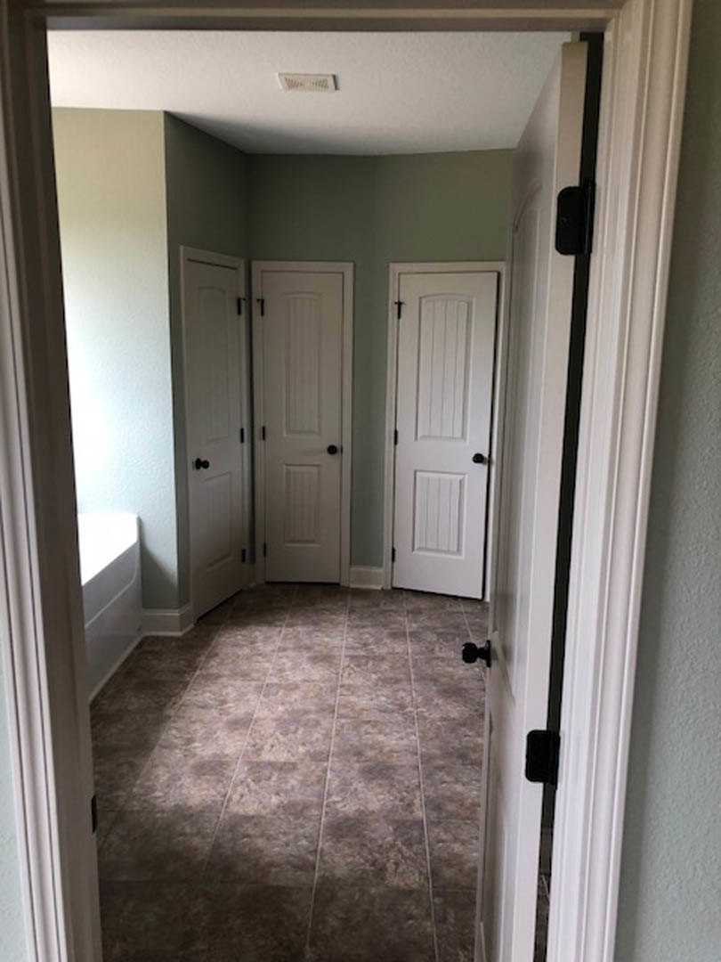 Bathroom with white paneled doors featuring black handles, freestanding bathtub, brown tile flooring, and natural light illuminating white walls and ceiling.