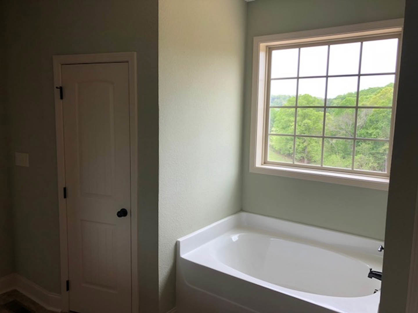 Freestanding white bathtub beneath large window, white walls, chrome faucet, minimalist bathroom design