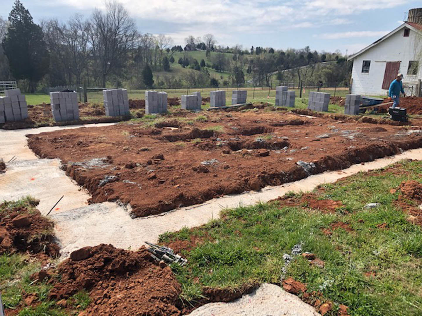 Partially built house with exposed framing and unfinished exterior walls, surrounded by green grass and scattered concrete blocks on construction site