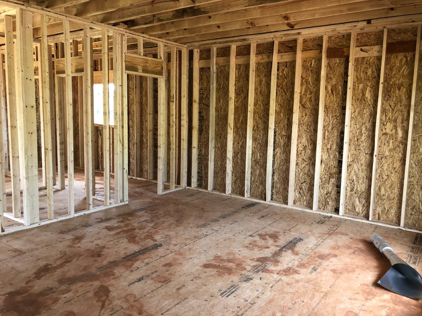 Unfinished room with exposed wood framing, lumber beams, and construction materials scattered on plywood floor