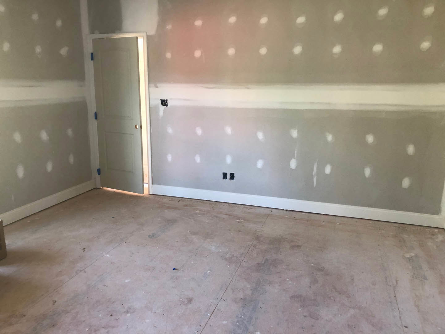White-painted wall and ceiling, white door with blue handle, tile flooring with visible dirt, minimalist interior with plaster finishes.