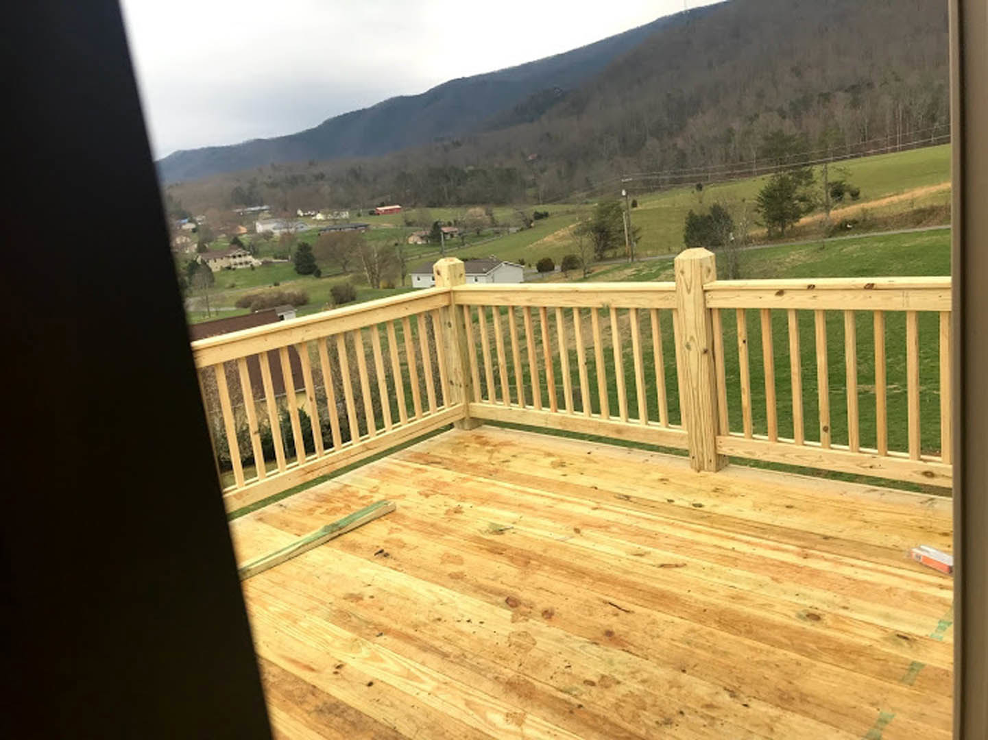 Wooden deck with railing overlooking grassy yard, valley, and distant mountain range under blue sky
