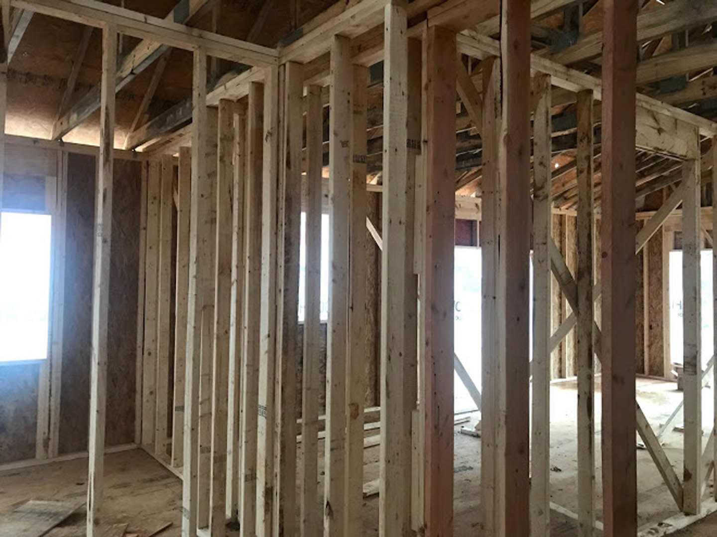 Exposed wood framing with vertical beams, partially installed window, unfinished interior walls, and construction materials scattered on subfloor