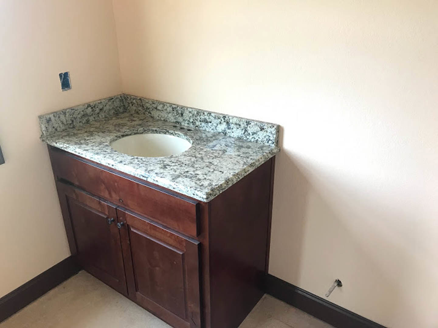 White undermount sink set in a granite countertop with chrome faucet, tile backsplash, and light wood cabinetry in a modern bathroom.