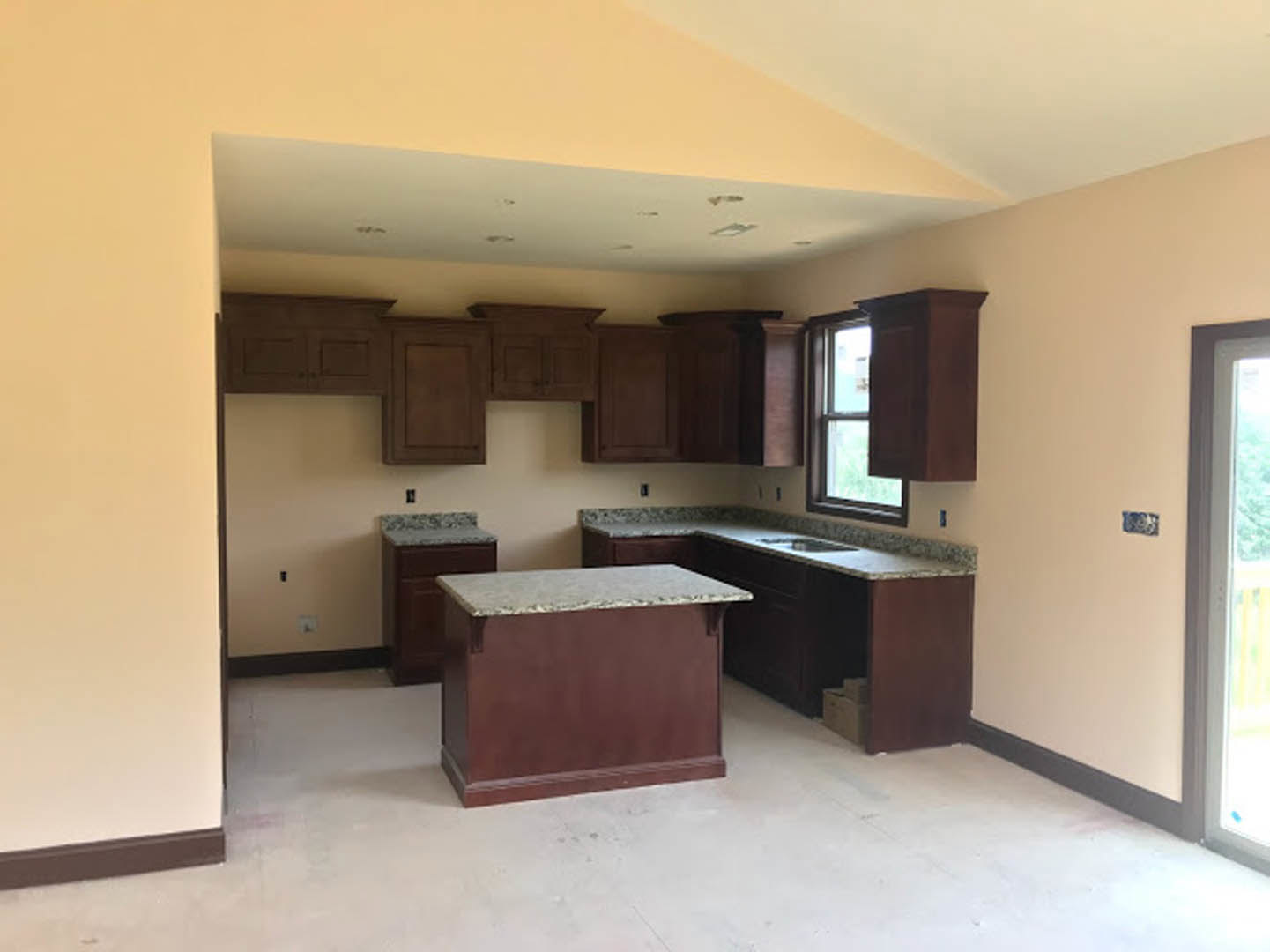 Granite countertops with brown cabinetry, stainless steel sink, and large window allowing natural light into the kitchen.