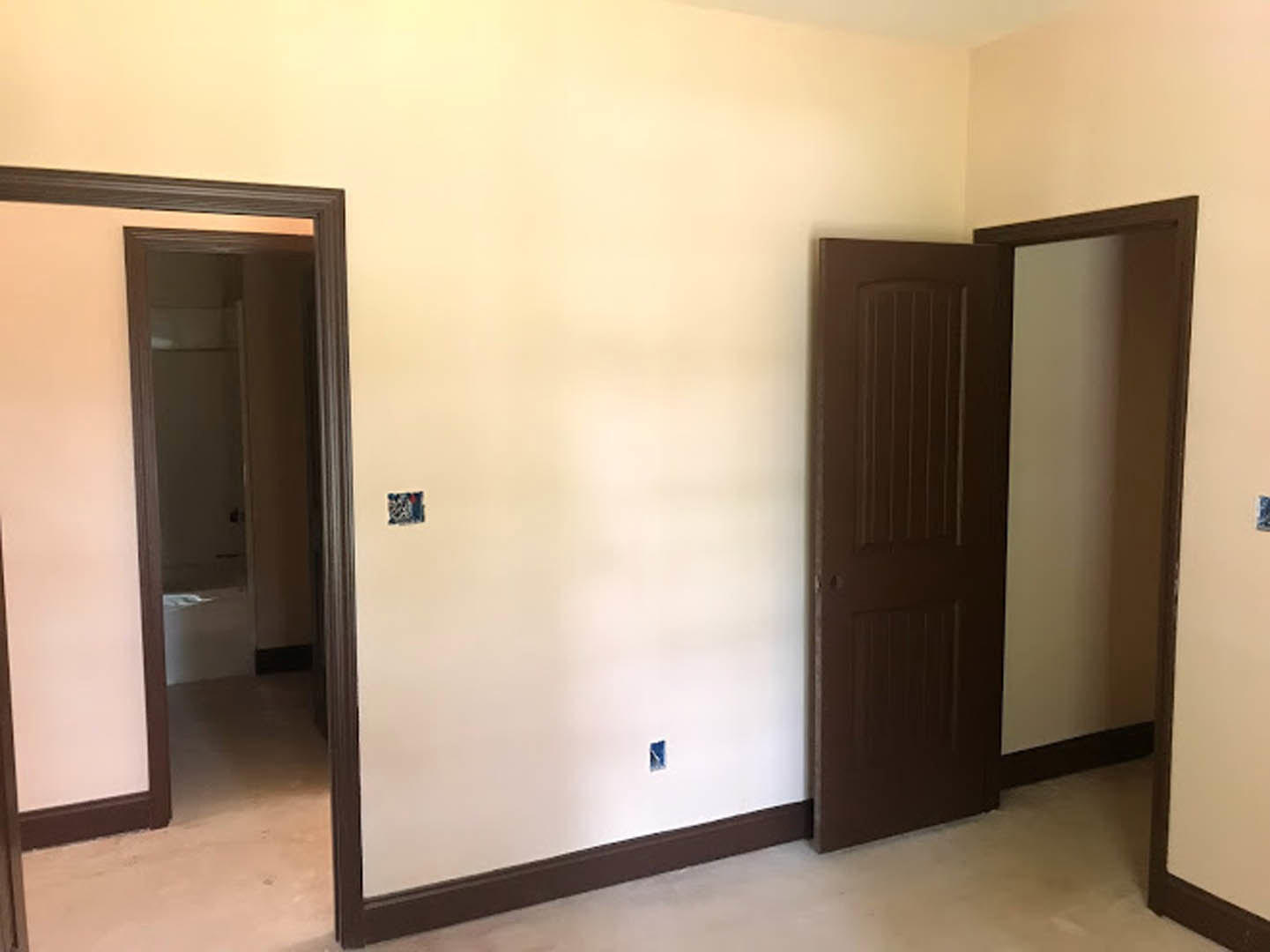 White-walled room with two wooden doors, light hardwood flooring, and a large wall mirror reflecting part of the interior.