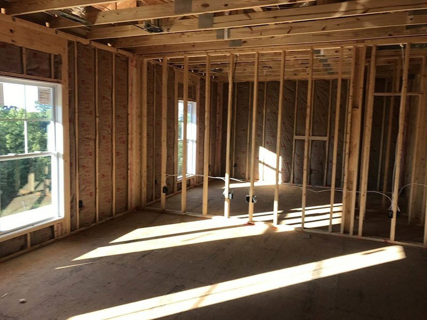 Living room with exposed wood ceiling beams, large windows overlooking trees, sunlight illuminating hardwood floors