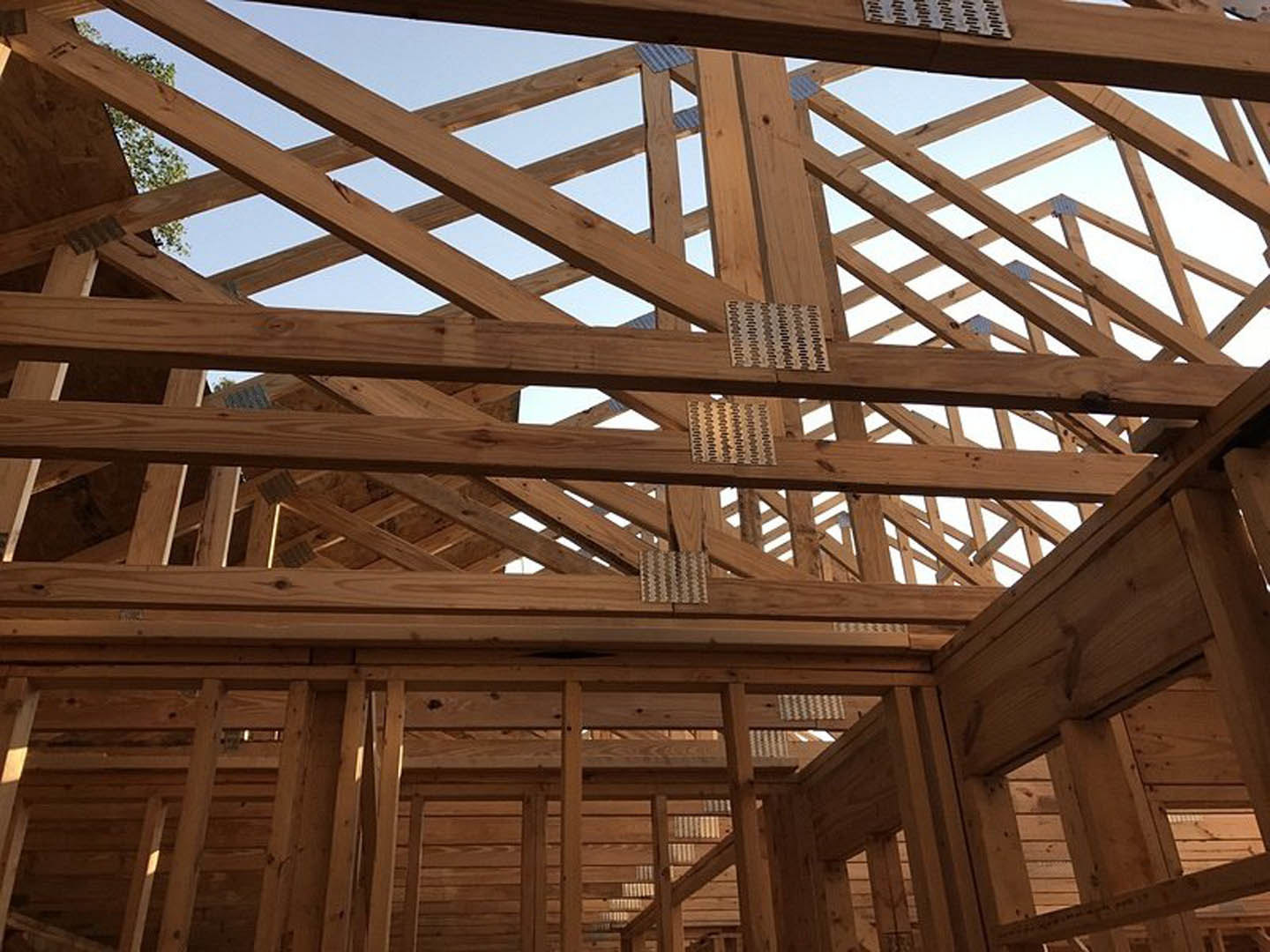 Exposed wood framing and beams inside a partially constructed house, natural daylight streaming through open window spaces