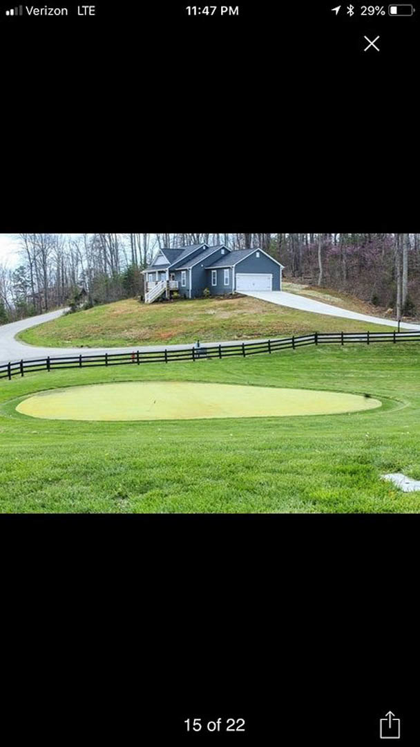 Modern home with attached garage situated on a grassy hill, black fence bordering the lawn, golf course and sand trap visible in the foreground, person standing near the sand trap.