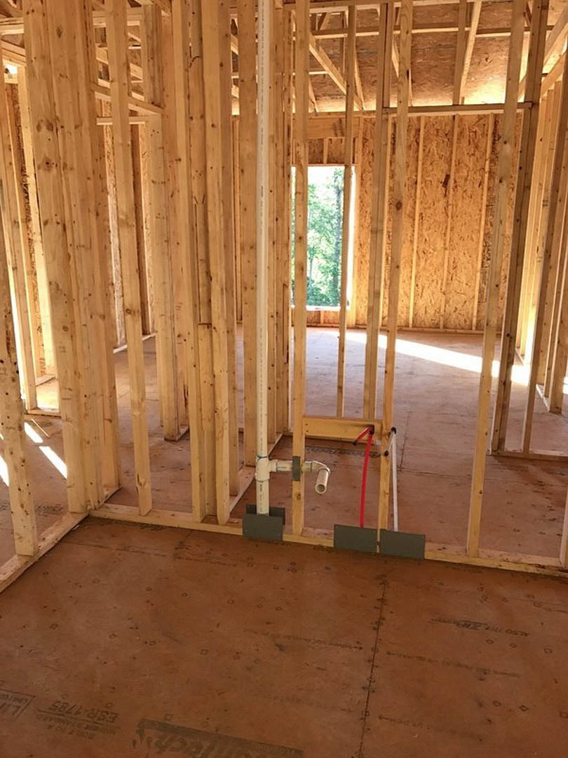 Wood-framed room under construction with exposed beams, unfinished walls, and a window revealing trees outside