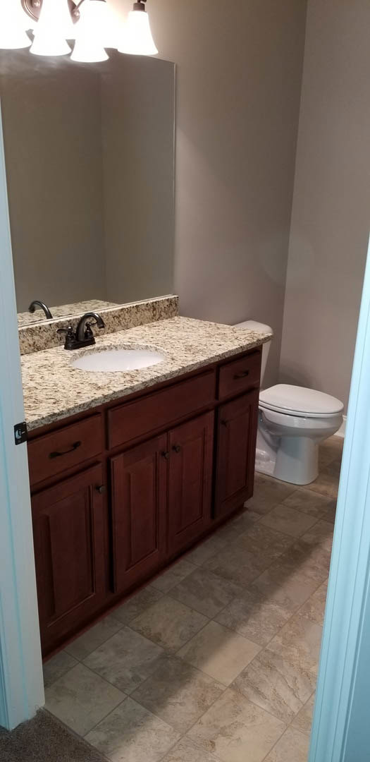 Bathroom with marble countertop vanity, undermount sink, chrome faucet, white toilet, wall-mounted mirror, light fixture, and neutral tile flooring