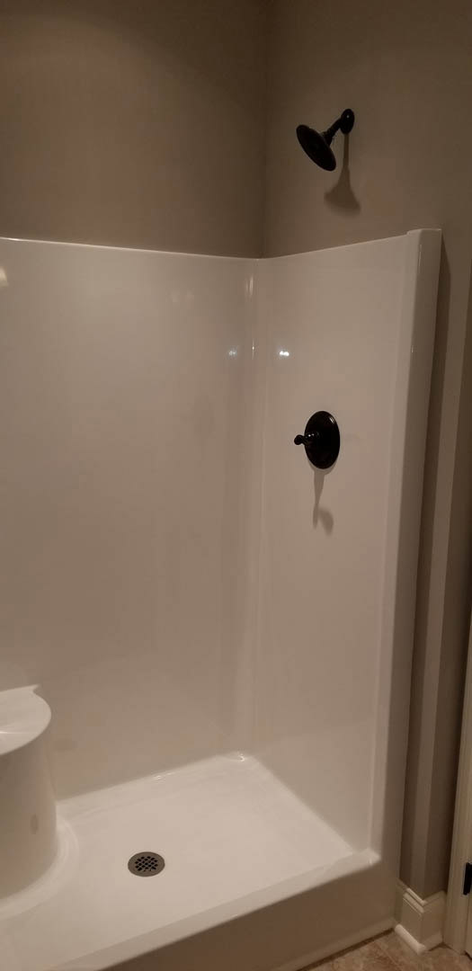 White tiled shower with black handle and faucet, white wall with subtle shadow