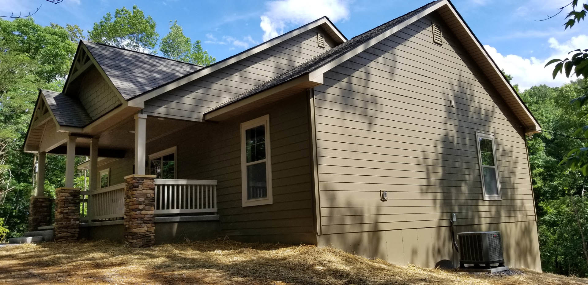 Two-story house with covered front porch, stone accent wall, white-framed windows, and landscaped yard with trees and plants