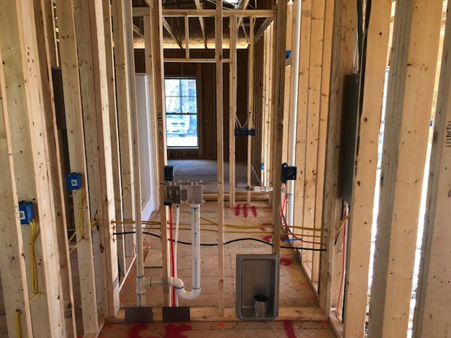 Framed interior of a house under construction with exposed wooden beams, insulation, unfinished floors, and a metal ladder.