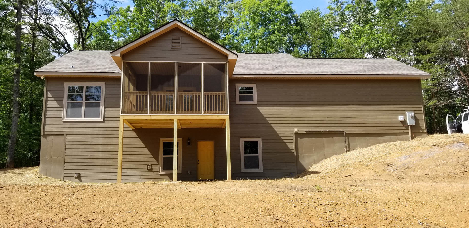 Two-story house with gray siding, white trim, covered front porch, yellow front door with porch light, attached garage, white-framed windows, landscaped yard with small tree