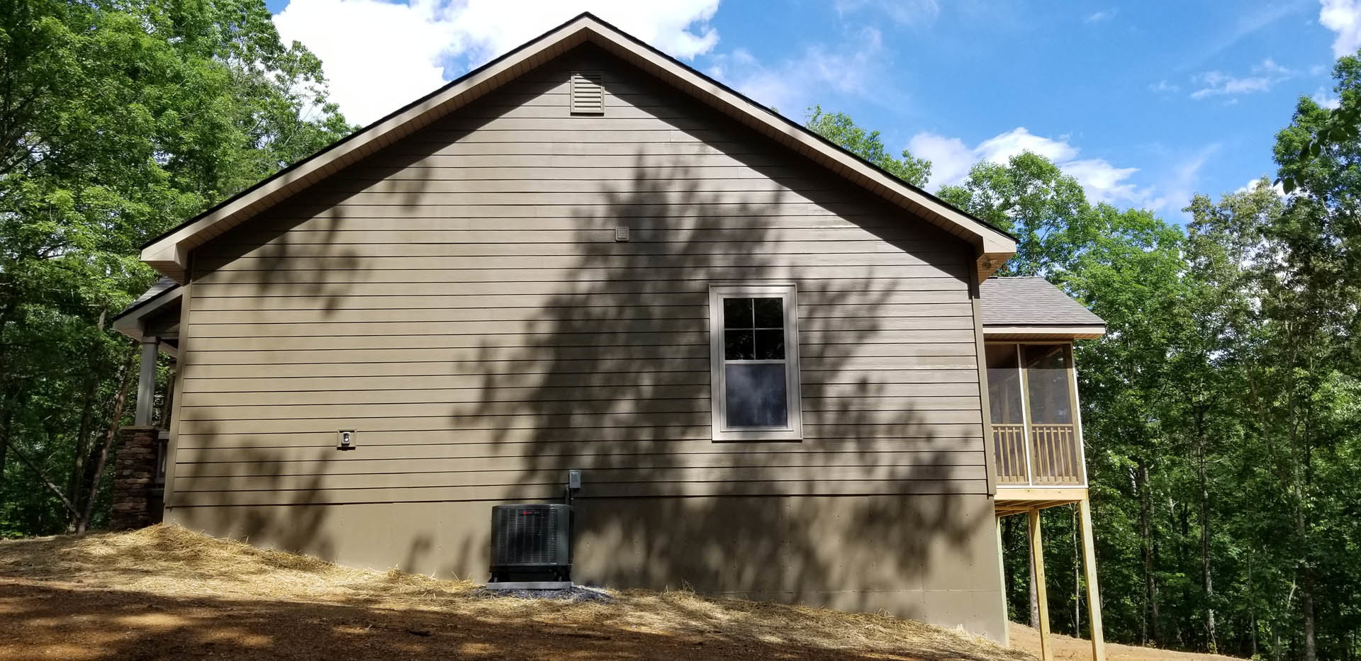 Two-story house with white-framed windows, balcony with metal railing, light-colored siding, and mature trees in the background