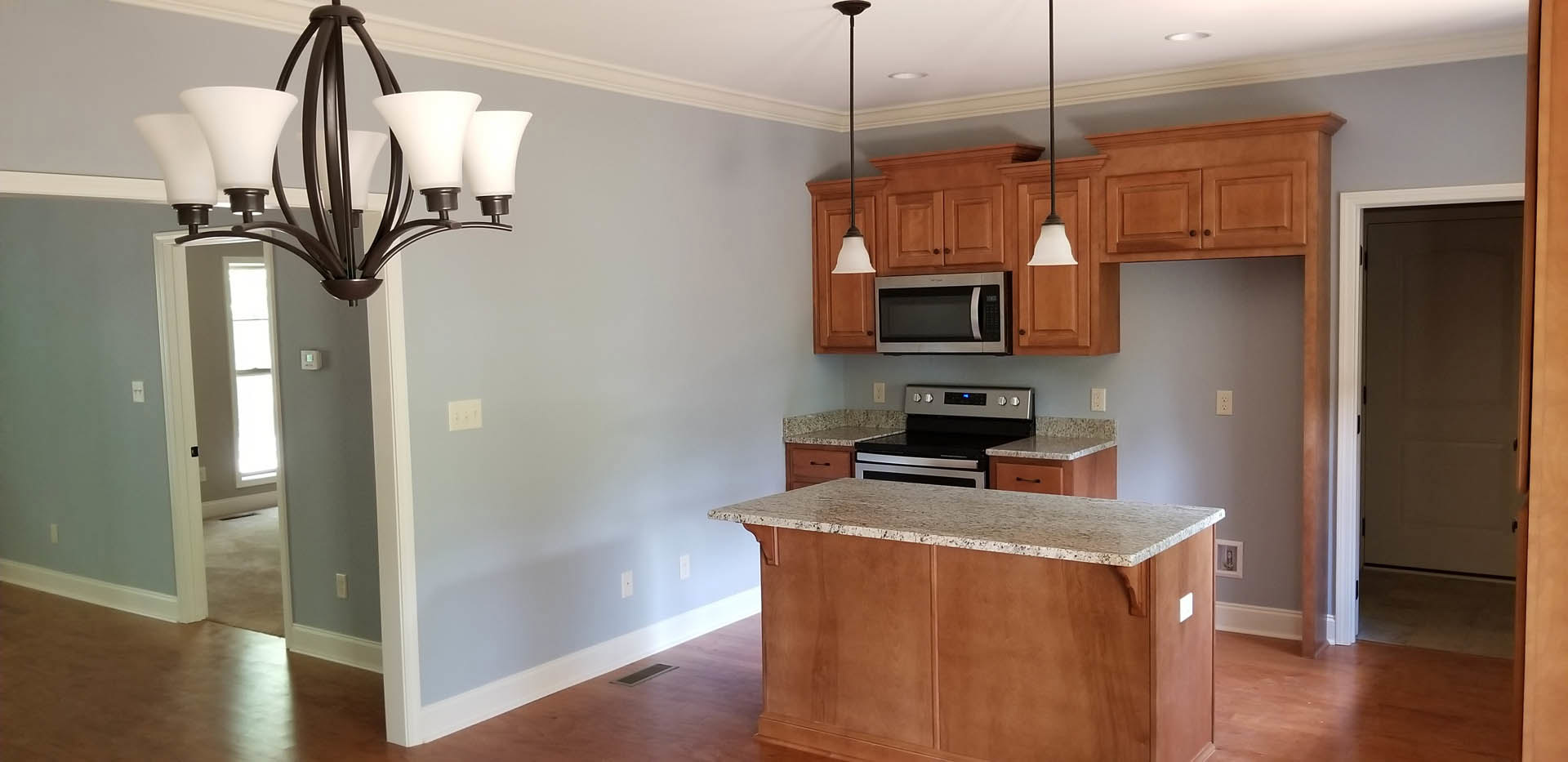 Marble kitchen countertop with open microwave, five-light chandelier, stove close-up, white light switch on wall, white cabinetry