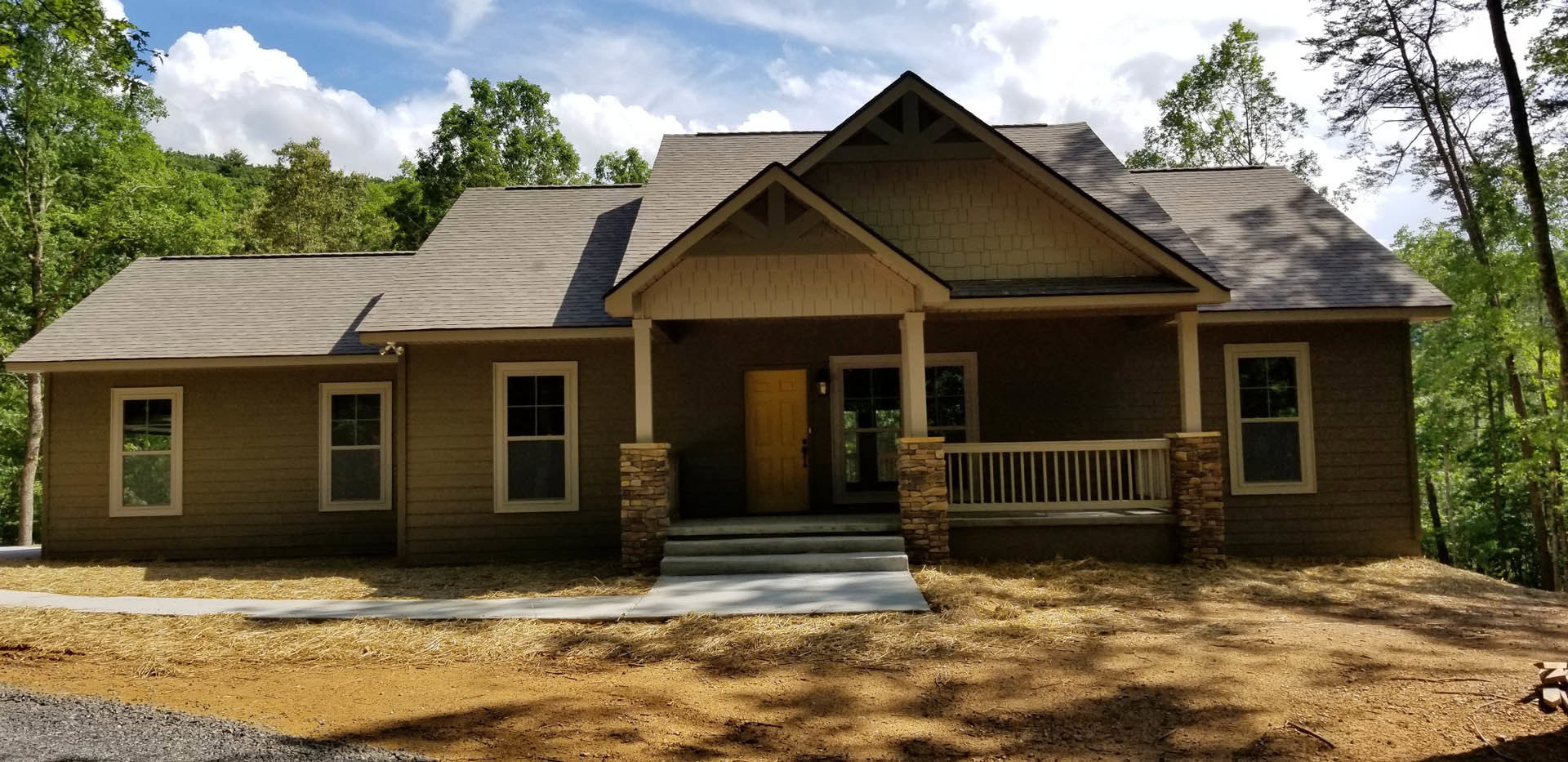 Yellow front door and white-framed window on a cottage-style home with two porches, white metal grate on exterior wall, surrounded by trees and sky