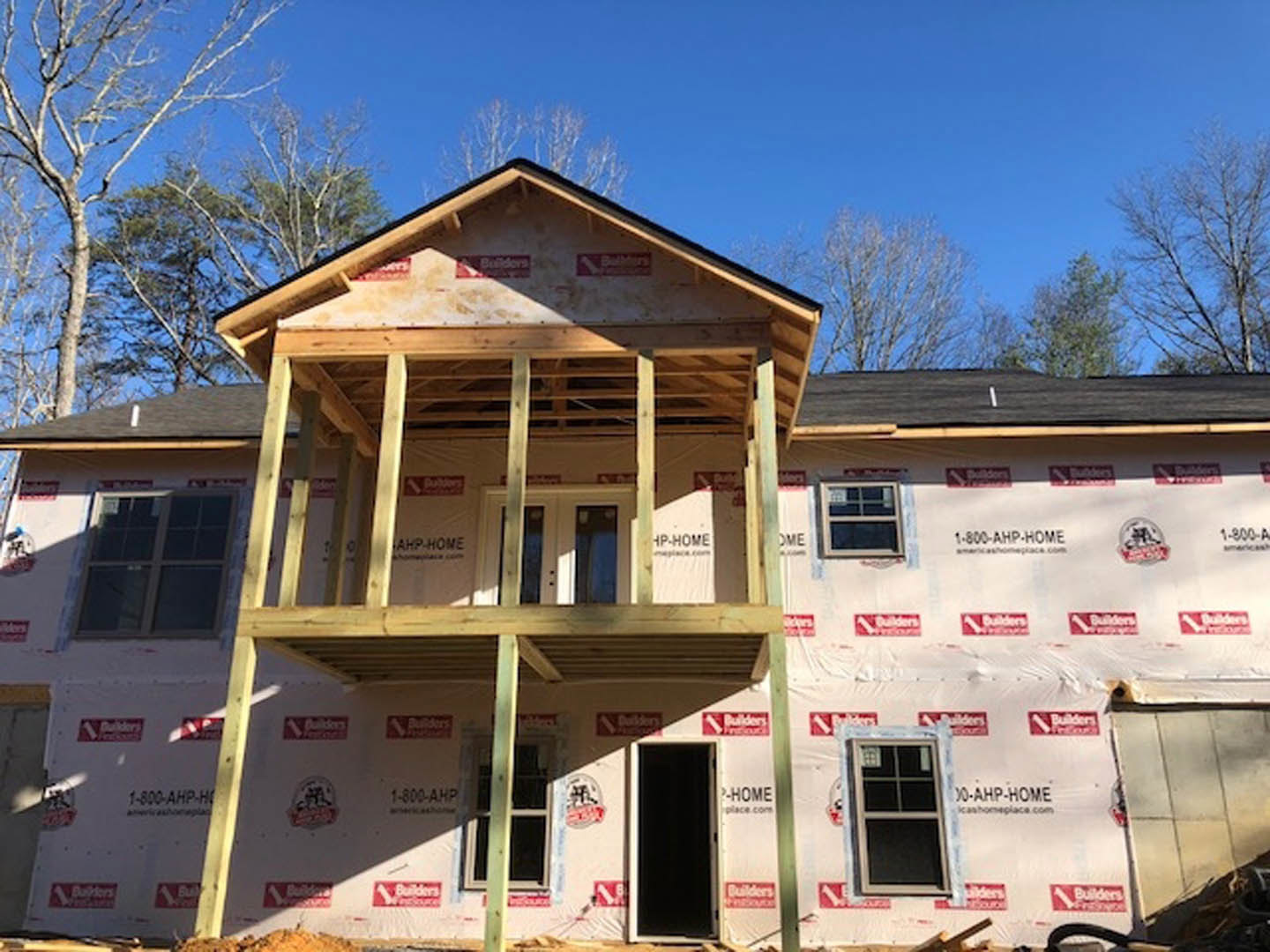 Partially finished house with white siding, black door, multi-pane windows, covered porch, and cartoon face drawn on exterior wall