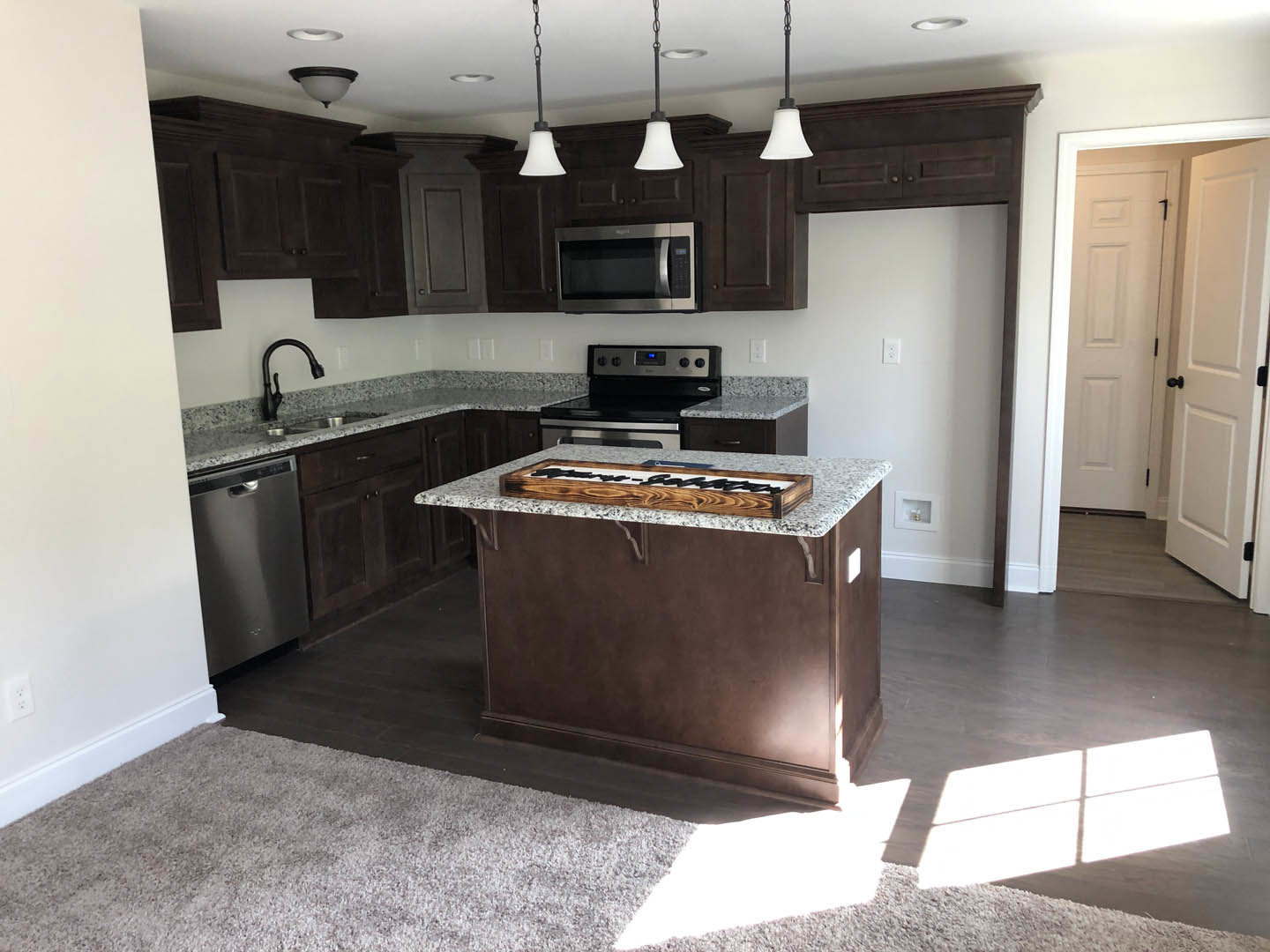 Kitchen with dark wood cabinets, marble island countertop, black faucet, stainless steel microwave, stove with digital display, and decorative sign on the counter