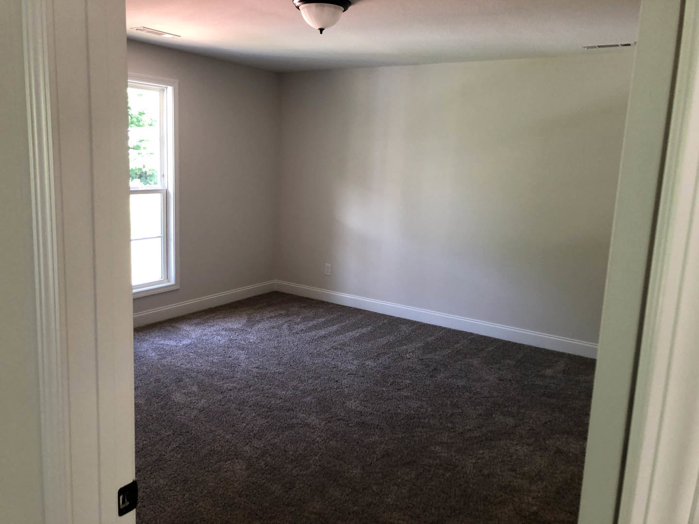 Carpeted room with white plaster walls, large window with white frame, ceiling light fixture, and neutral finishes