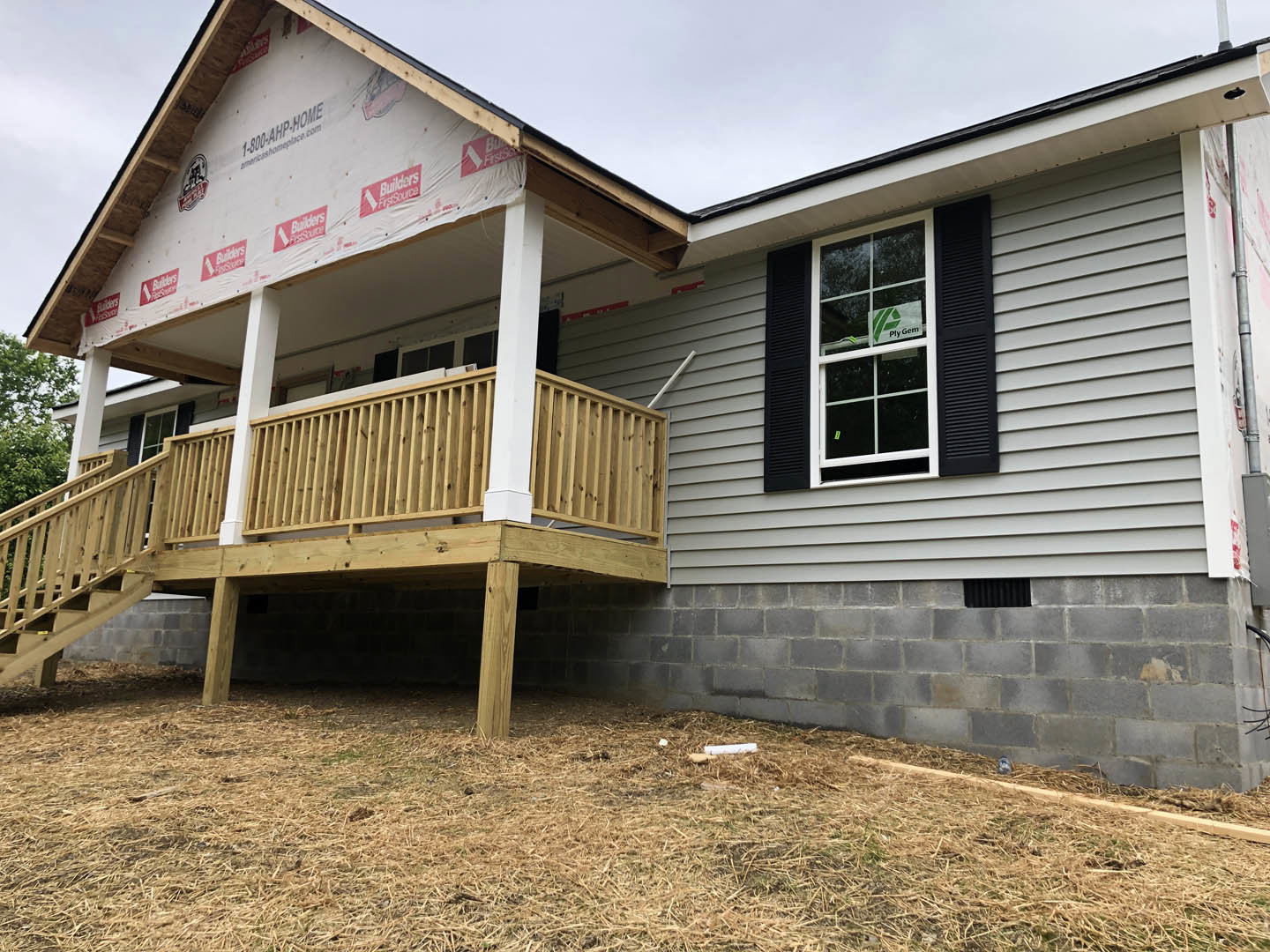 White cottage-style home with wooden porch, black shutters, horizontal siding, red and white sign in window, and spacious outdoor deck