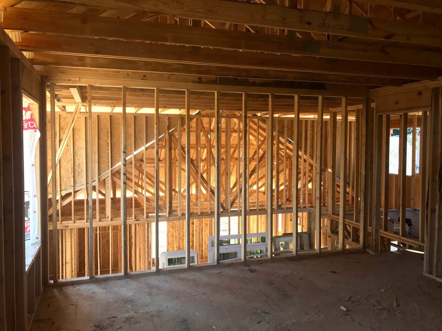 Open-concept room featuring a full wall of vertical wood planks, exposed ceiling beams, concrete floor, and large window letting in natural light