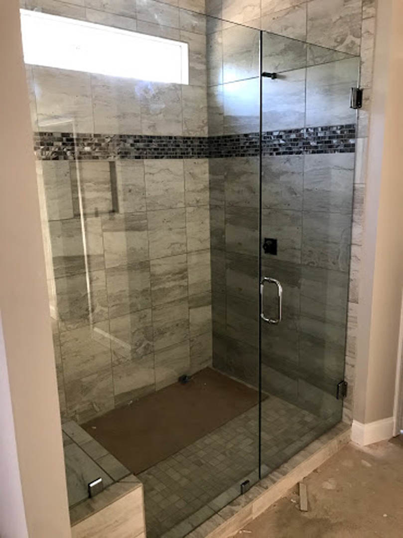 Glass shower enclosure with chrome fixtures, marble tile floor, and wall-mounted mirror in modern bathroom.