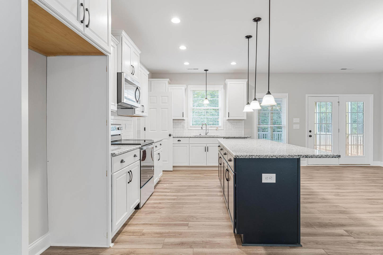 White kitchen cabinets and black marble-topped island, glass-paneled double doors, white framed door, ceiling light fixture, hardwood flooring